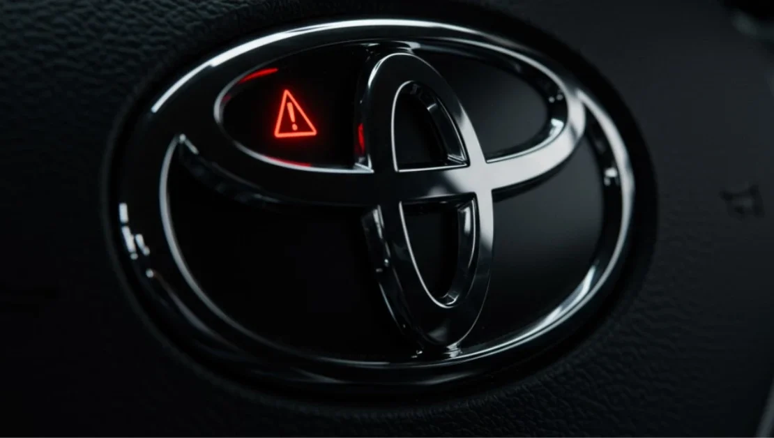 A sleek, modern Toyota steering wheel emblem with the reflection of a red dashboard warning light, symbolizing the urgent Toyota Recall 2025 for a critical airbag sensor defect.